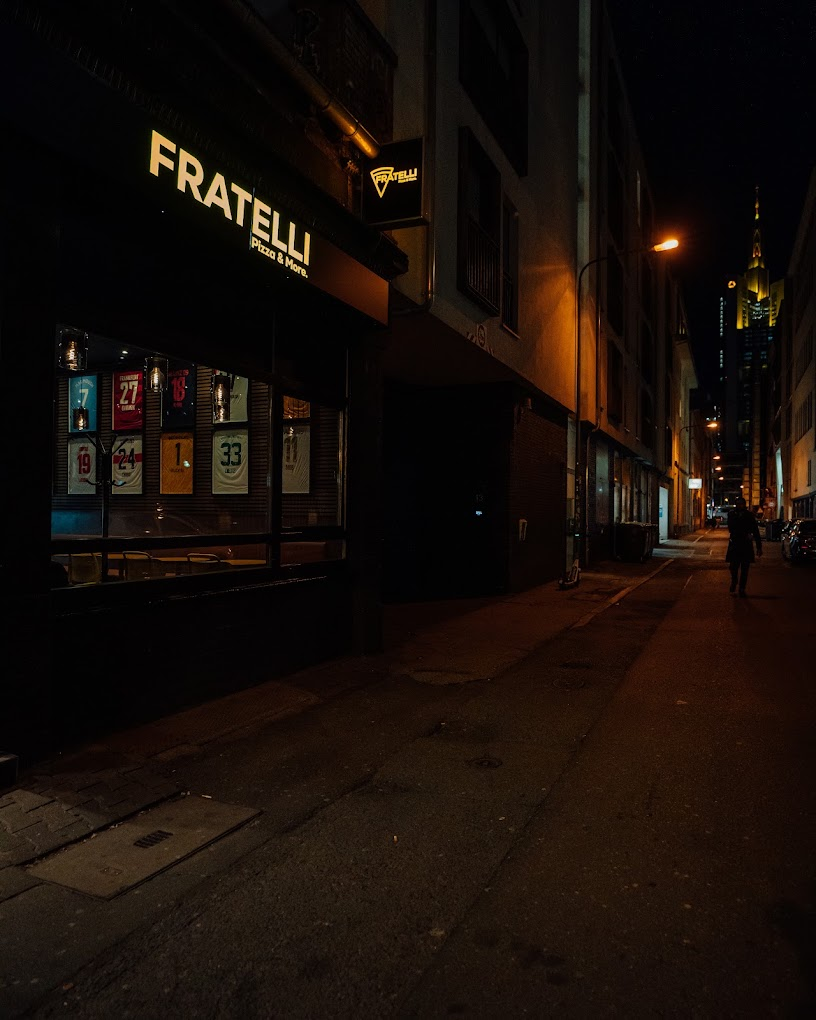Die echte Fratelli-Fassade mit beleuchtetem Schild und Frankfurter Straße bei Nacht